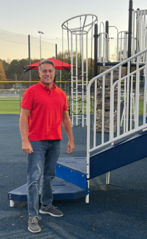 A man in a red polo shirt stands on a playground.
