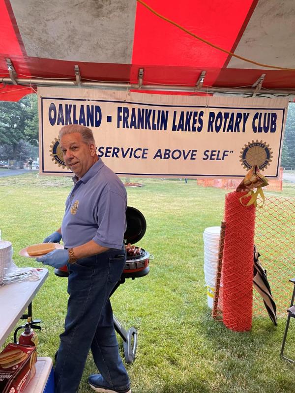 A man in blue shirt serving hot dogs in a tent with a Rotary banner
