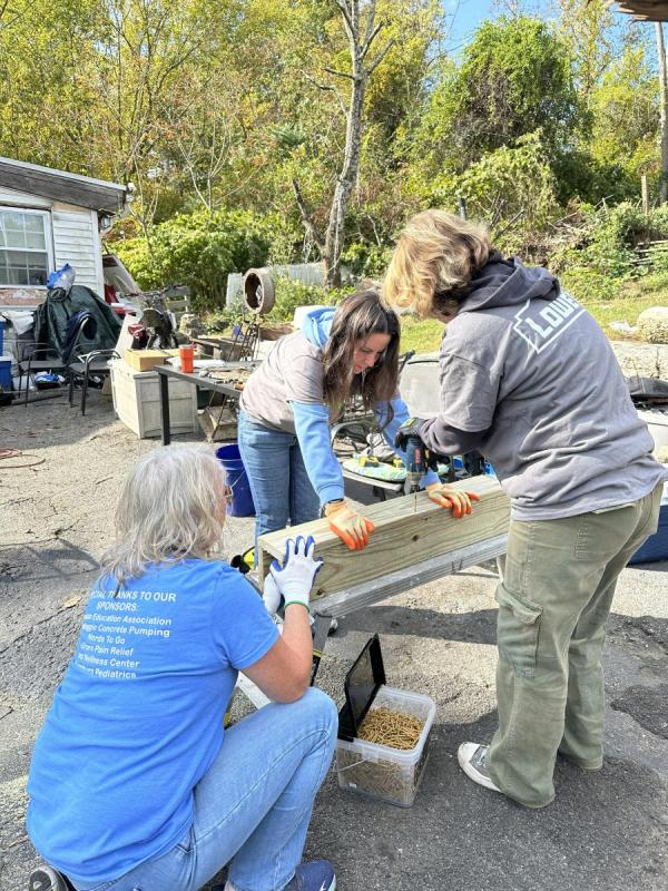 Three women use a power drill to set large screws.