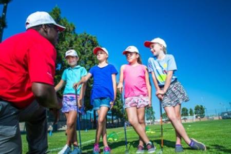 A coach works with four kids leaning to play golf.